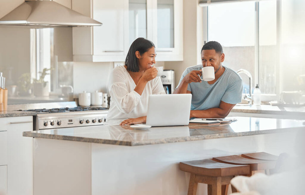 a couple drinking coffee while using a laptop in the kitchen at home. - Foto, Imagem