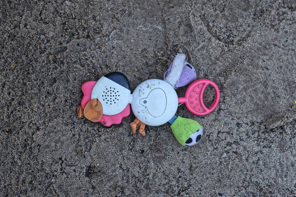 one colored plastic fabric toy rattle lies in the gray sand of the sandbox on the street - Foto, imagen