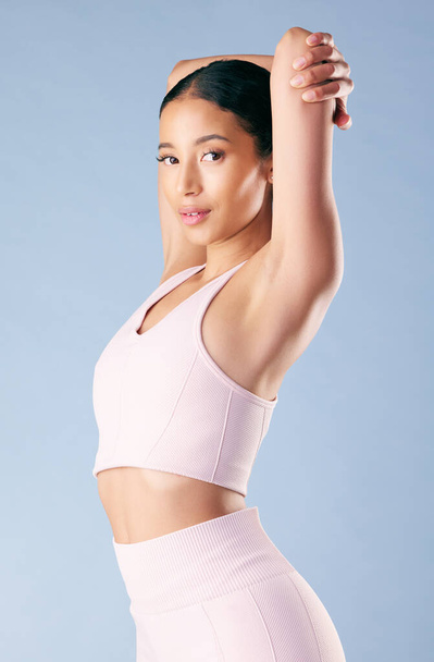 Mixed race fitness woman stretching in studio against a blue background. Beautiful young hispanic female athlete warming up for exercising or working out. Dedicated to a fit and healthy lifestyle. - Fotó, kép