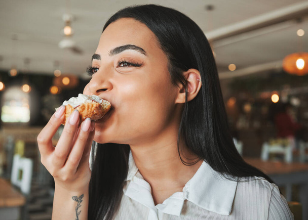 a beautiful young woman biting into a tasty treat in a cafe. - Photo, image