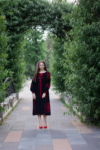 portret van een jonge vrouw in zwart en rood vyshyvanka. nationaal geborduurd Oekraïens shirt. meisje in jurk buiten in het park. zomer. - Foto, afbeelding