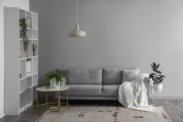 Interior of light living room with grey sofa, table and shelving unit - Valokuva, kuva