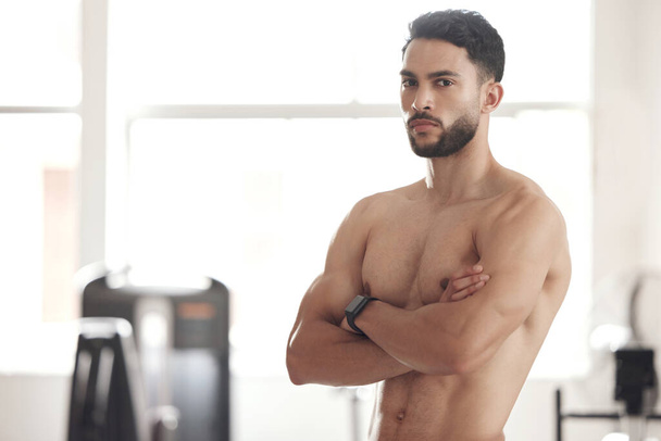 Portrét jednoho mladého nahého hispánského muže s velkými silnými svaly z pravidelného cvičení, který stojí se zkříženýma rukama v tělocvičně. Vážný kulturista s tónovanou a sexy postavou. Brawny atlet hrdý - Fotografie, Obrázek