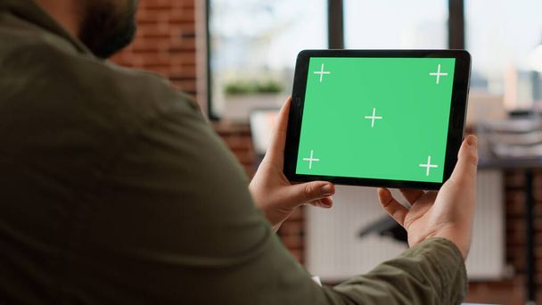 Office worker holding horizontal greenscreen on tablet, analyzing chroma key display with isolated mockup on background. Looking at digital gadget with blank copyspace template. Tripod shot. - 写真・画像