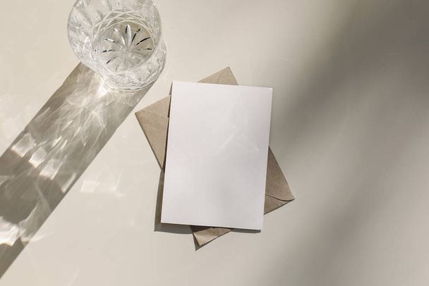 Summer stationery still life. Modern minimal composition. Greeting card, invitation mock up scene with envelope. Drink glass, long harsh shadows overlay, beige table background in sunlight. Flat lay. - Photo, image