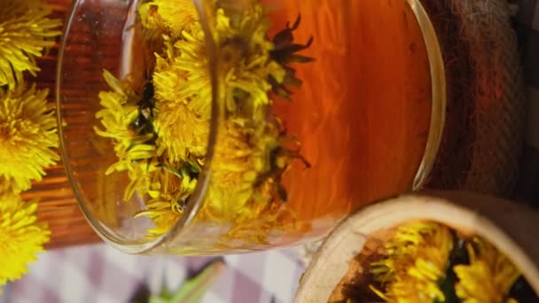 Dandelion flower healthy tea in glass teapot and glass cup on table. Delicious herbal tea pouring from fresh dandelion flowers at home at summer day near garden. Vertical footage Green clearing Hot - Imágenes, Vídeo