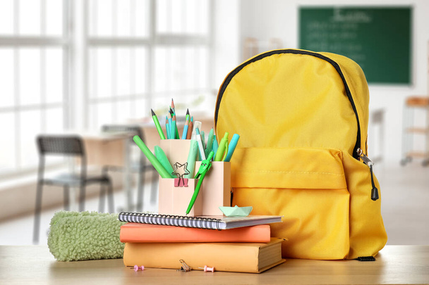 Set of school stationery and backpack on table in classroom - Фото, изображение