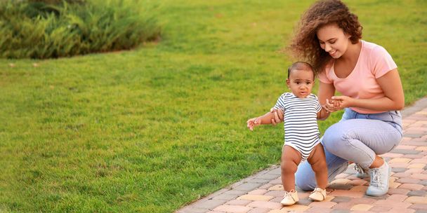 African-American woman teaching her little baby to walk outdoors - Фото, изображение