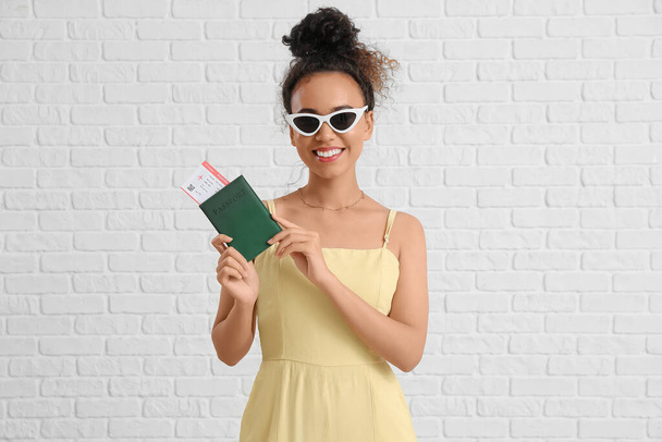 Młoda Afroamerykanka z paszportem i biletem na tle białej cegły - Zdjęcie, obraz