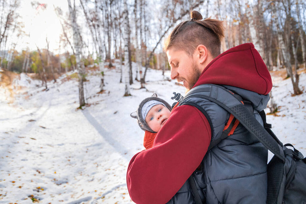 The baby walks through the winter forest in the arms of his babywearing father. - Fotografie, Obrázek