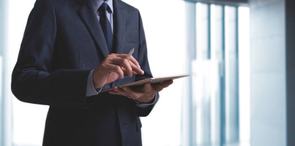 Biznesmen, przystojny mężczyzna w czarnym garniturze i krawacie ze stojącym piórem rysika, korzystający z tabletu cyfrowego w nowoczesnym biurze, mnóstwo miejsca do kopiowania dla biznesu i technologii - Zdjęcie, obraz