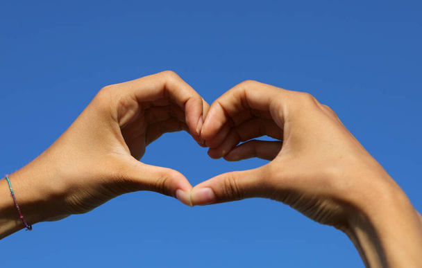 two joined hands of a person forming a big heart and the blue sky background - Foto, afbeelding