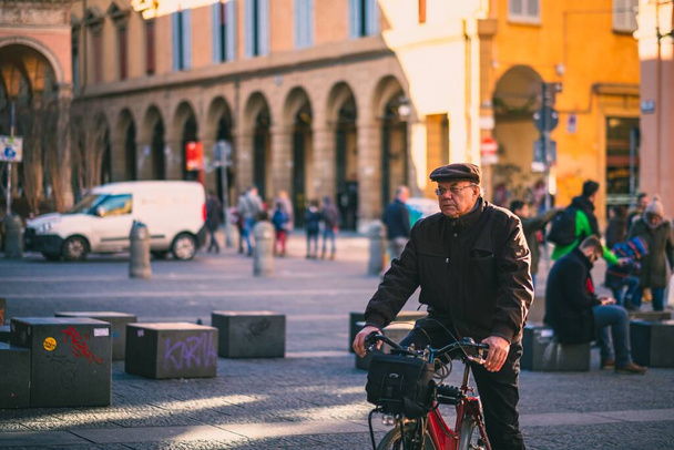 An adult man on a bicycle cycling past a town square in Bologna, Italy - Фото, зображення