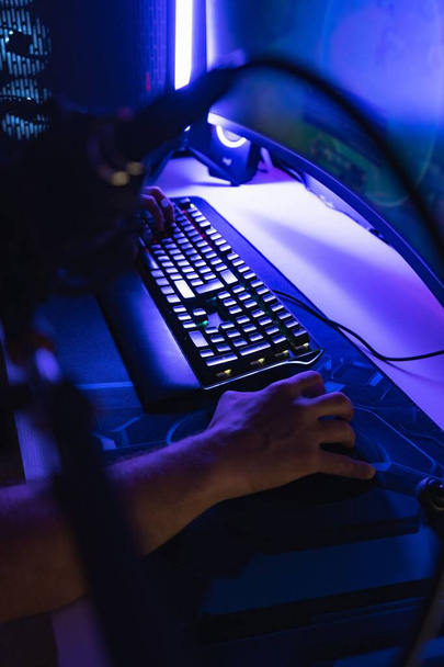 A vertical shot of hands on a mouse and keyboard playing a game on a PC in a room with blue light - Fotó, kép