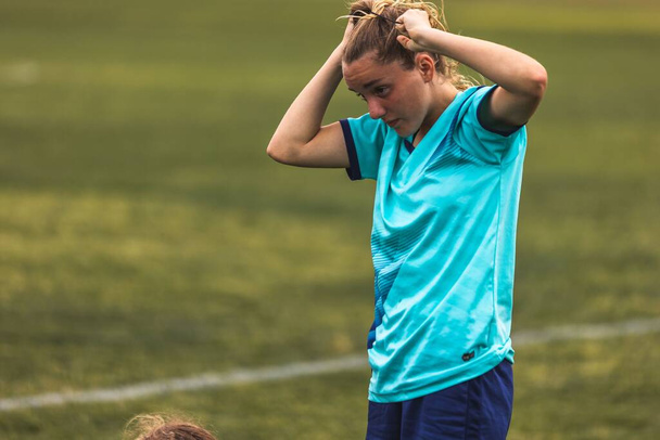 A young female player fixing her hair during the game at Youth Soccer Game - Zdjęcie, obraz