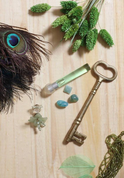 Eine vertikale Aufnahme eines alten Schlüssels mit Parfüm, Schmuck und Pfauenfedern auf einem Holztisch - Foto, Bild