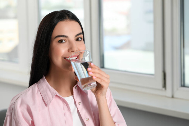 Young woman drinking water indoors, space for text. Refreshing drink - Foto, Bild