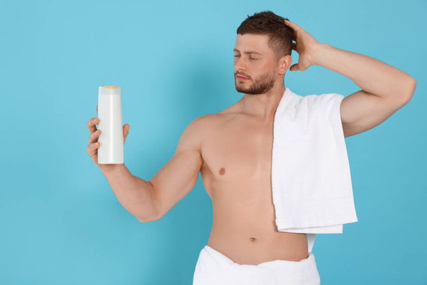 Shirtless young man holding bottle of shampoo on light blue background - Zdjęcie, obraz