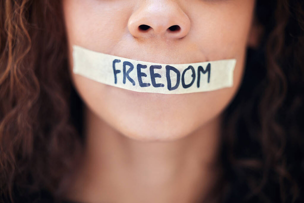 Ujęcie z bliska nierozpoznawalnej kobiety z taśmą na ustach z napisem "wolność". - Zdjęcie, obraz