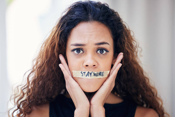 Portrait of a young woman with tape on her mouth that has the words stay woke written on it. - Foto, Imagem
