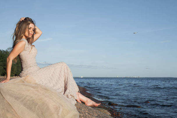 Прекрасна жінка в бежевій сукні на узбережжі моря
 - Фото, зображення