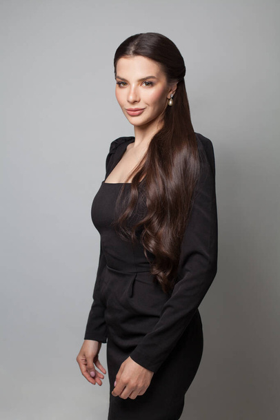 Fashion portrait of beautiful young woman in black dress standing on grey background - Zdjęcie, obraz