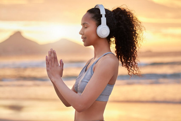 a woman wearing headphones while practising yoga on the beach. - 写真・画像