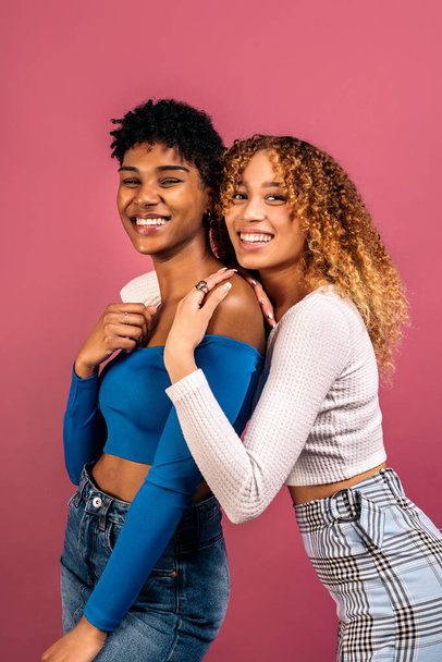 Stock photo of cheerful afro women hugging each other in studio shot against pink background. - Фото, зображення