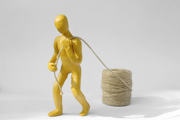 Human figure made of yellow plasticine carrying rope on white background - Valokuva, kuva