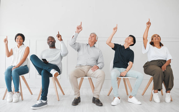 a diverse group of people pointing up while sitting in line against a white background. - Fotó, kép