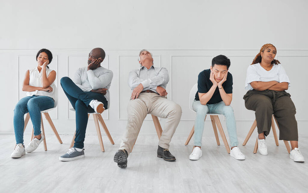 a diverse group of people looking bored while sitting in line against a white background. - Foto, imagen
