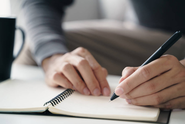 Ο αριστερόχειρας γράφει σε ένα σημειωματάριο στο τραπέζι. - Φωτογραφία, εικόνα