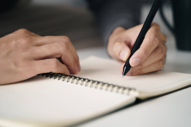 linkshandige man schrijft in een notitieboekje op tafel - Foto, afbeelding