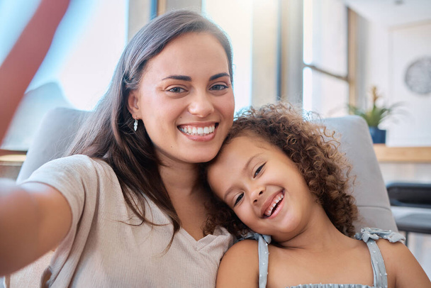 Detailní záběr hispánské matky a malé dcery s úsměvem při užívání selfie. Šťastná mladá maminka baví a přičemž autoportrét s rozkošnou dceru doma. - Fotografie, Obrázek