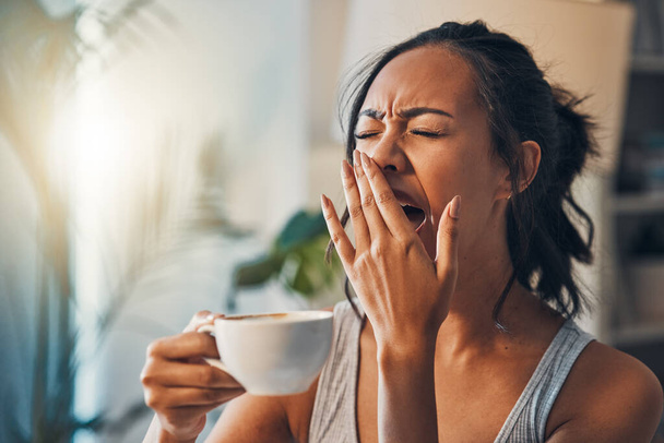 A young mixed race woman yawning while lying in bed and drinking coffee. An attractive Hispanic female waking up from a her sleep and getting ready to begin her day. - Φωτογραφία, εικόνα
