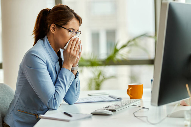 Молода бізнес-леді, яка має вірус грипу і використовує тканину, дме ніс в офісі
.  - Фото, зображення