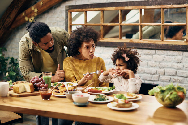 African American parents feeding their daughter who is refusing to eat vegetables at dining table.  - Photo, Image