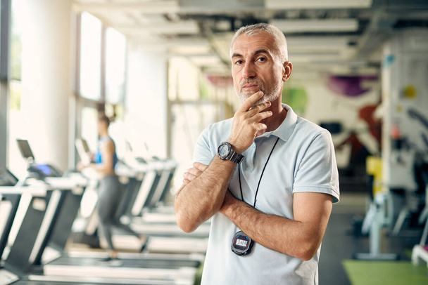 Portrait of mature personal trainer with hand on his chin standing in health club and looking at camera.  - Foto, Imagem