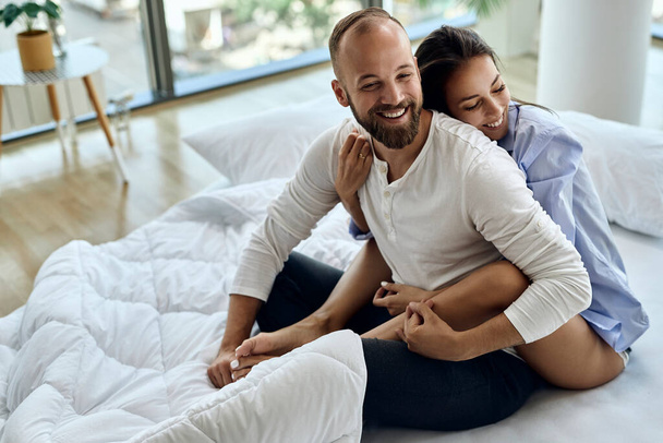 Young happy couple sitting embraced on a bed and having fun in the morning.  - Foto, Bild