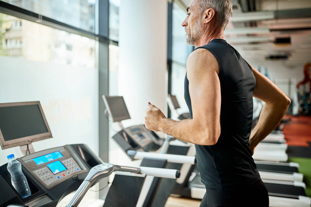 Mature athletic man running on treadmill during sports training in a gym.  - Foto, Bild