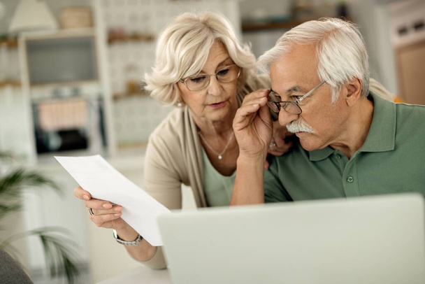 Senior man and his wife using laptop while going through their finances at home. - Foto, Bild