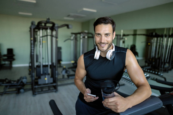 Happy athletic man relaxing after running on treadmill and using cell phone in a gym.  - Fotoğraf, Görsel