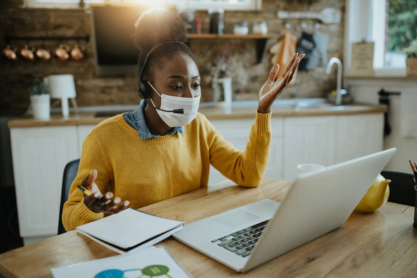 Bilgisayar kullanırken koruyucu yüz maskesi takan siyahi kadın girişimci evden internet üzerinden toplantı yapıyor..  - Fotoğraf, Görsel
