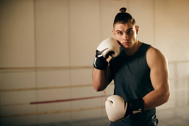 Boks kulübündeki spor eğitimi sırasında boks eldivenli genç erkek dövüşçünün portresi.. - Fotoğraf, Görsel