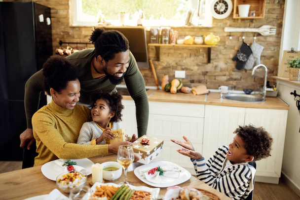 Happy black kids receiving Christmas presents form their parents during family lunch at home.  - Фото, зображення