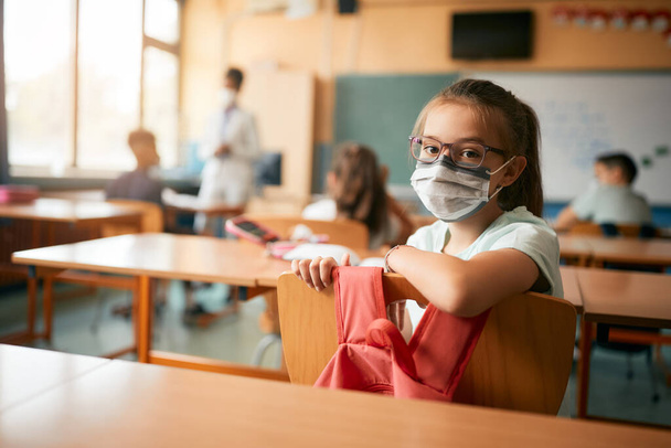 Elementary student looking at camera during a class and wearing face mask due to coronavirus pandemic.  - Photo, Image