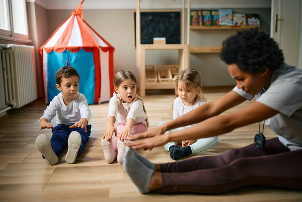African American teacher and group of children doing stretching exercises on the floor at kindergarten.  - Photo, image