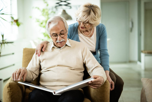 Старший чоловік і його дружина дивляться фотографії в сімейному альбомі вдома
.  - Фото, зображення
