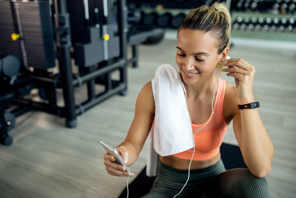 Happy athletic woman using mobile phone while relaxing after sports training in a gym.  - Foto, Imagem