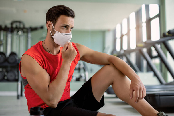 Athletic man adjusting face mask while preparing for a workout in health club during virus epidemic.  - Valokuva, kuva